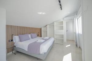 a white bedroom with a large bed with purple pillows at Principado de Aracena I in Aracena