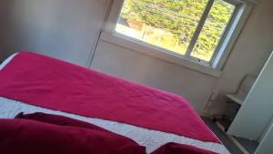a bed with a pink blanket sitting next to a window at Hostal Posada Lupinos in Punta Arenas