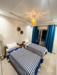 two beds in a room with blue curtains at 2BR Pool View Kids Pool & Gym 6 Min to Beach in Dar Hamida