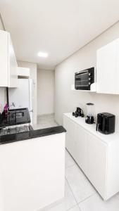 a white kitchen with white cabinets and black appliances at Apartamento Aconchegante de 02 Quartos in Cuiabá