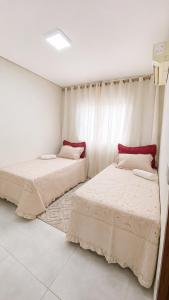 two beds in a room with white walls at Apartamento Aconchegante de 02 Quartos in Cuiabá