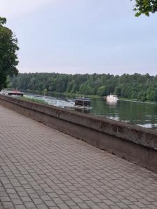 a river with two boats in the water and a sidewalk at Amber Stay Birštonas in Birštonas