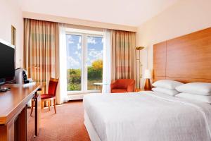 a hotel room with a bed and a desk and a window at Sheraton Duesseldorf Airport Hotel in Düsseldorf