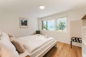 a white bedroom with a bed and a window at FLORA BAY Spacious Lake and Mountain View Apartment in Niederried