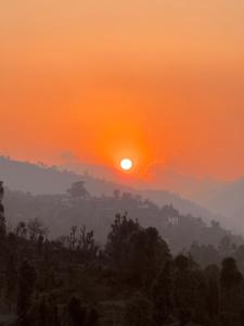 an orange sunset with the sun in the sky at THHPSOCIETY - Exstacy stays & cafe - Your Romantic & Cozy Getaway - Mountain view , Hot tub , Parking - MUKTESHWAR in Mukteshwar +219 photos