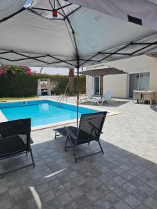 a swimming pool with two chairs and an umbrella at Villa Wissal Djerba piscine privée in Arkou +6 photos