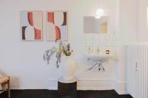 a white bathroom with a sink and a vase with flowers at Nomad Hotel - Frederiksberg in Copenhagen