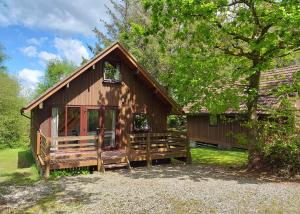 a wooden cabin with a porch and a tree at Eastcott Lodges in North Tamerton