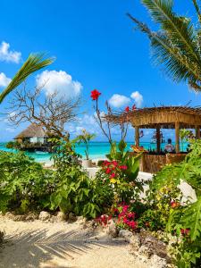 a beach with flowers and a pavilion and the ocean at Villa Duara Zanzibar Rooftop Infinity Pool The Rock View in Michamvi +10 photos