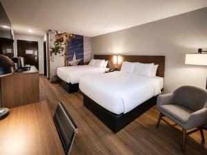 a hotel room with two beds and a chair at Clarion Pointe Addison - Dallas North in Addison