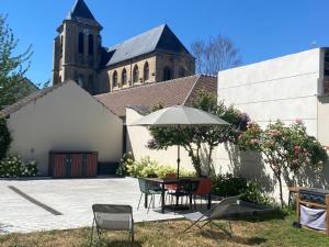 a table and chairs with an umbrella in front of a church at Lilau - Villa de charme avec parking et jardin près de Chantilly in Gouvieux