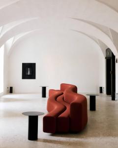 a red chair in a white room with two tables at Palazzo Daniele, a Member of Design Hotels in Gagliano del Capo