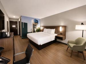 a large hotel room with a bed and a chair at Clarion Pointe Addison - Dallas North in Addison