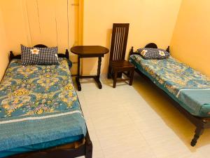 a room with two beds and a table and a chair at Akkaraipattu Guest House in Akkaraipattu
