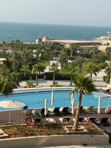 a pool with chairs and palm trees and the ocean at Inter Home Coral - beach access in Ras al Khaimah