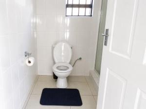a bathroom with a toilet with a window and a rug at R&N Hosts in Maseru
