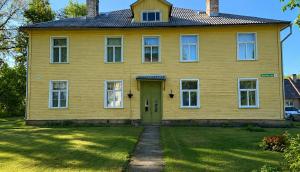 a yellow house with a green door in a yard at Taevaskoja külaliskorter in Taevaskoja