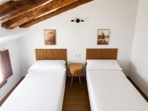 two beds in a room with white walls and wooden ceilings at Origen&Madera in Alcalá del Júcar +3 photos