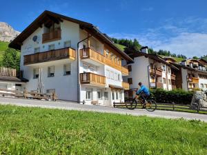 a person riding a bike down a road next to a building at Apartments Alpenroyal Arabba - Check-in at Garni Royal in Arabba