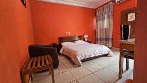 a bedroom with orange walls and a bed and a desk at Hôtel Cauris d'Or de Bouaké in Bouaké