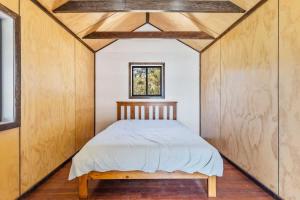a bed in a room with wooden walls and a window at Davali at Mogo in Mogo