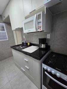 a kitchen with white cabinets and a stove and microwave at Casa 24 m2 aconchegante com AC in Sorocaba