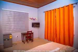 a bedroom with an orange curtain and a table at Le Mia KD lodge in Sekondi-Takoradi
