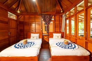 two beds in a room with wooden walls and windows at Welly Bungalow in Gili Trawangan