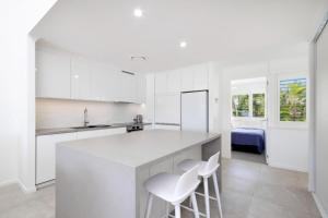 a white kitchen with white cabinets and white stools at Noosa Haven Apt 12 Riverfront Elegance in Noosaville
