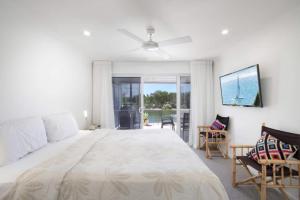 a white bedroom with a large bed and a balcony at Noosa Haven Apt 12 Riverfront Elegance in Noosaville