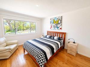 a bedroom with a bed and a chair and a window at Harbour Haven - steps from Ulladulla Harbour in Ulladulla