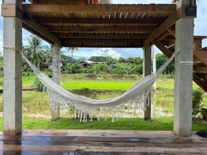 a hammock hanging from a porch in front of a field at Nonnatatonview นอนนาตาทนวิว in Phayao