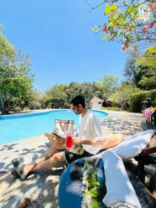 a man sitting on a couch next to a pool at The Hideaway Hosur by evaddo stays in Hosūr
