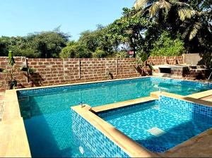 a large blue swimming pool with a brick wall at The Mamta Courtyard Anjuna in Anjuna