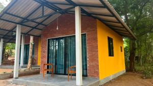a small house with a yellow wall and two chairs at Elevara Eco Resort - Wasgamuwa in Kathurupitiya