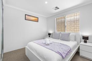 a white bedroom with a bed and a window at Alkimos Coastal Escape in Alkimos