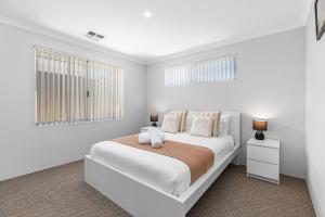 a white bedroom with a large bed and two windows at Alkimos Coastal Escape in Alkimos