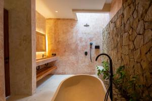 a bathroom with a tub and a stone wall at Sereno Lombok Resort in Selong Belanak