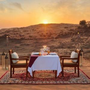 a table with two chairs and a table with a sunset at Sam Sand Dunes Camps Jaisalmer in Sām