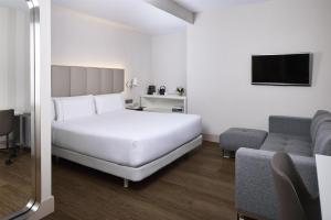 a bedroom with a white bed and a couch at NH Sants Barcelona in Barcelona