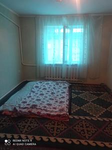 a bedroom with a bed with a window and a rug at Гостевой дом Izat in Karakol