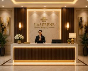 a woman standing behind a reception desk in a lobby at Hotel La Serene in Agra