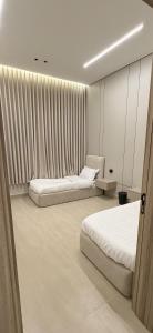 two beds in a room with white walls and curtains at Elite Stay in Buraydah