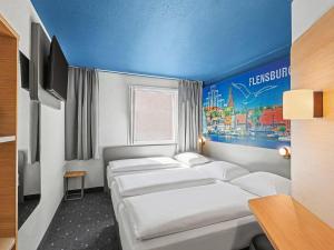 a room with three beds and a painting on the wall at B&B HOTEL Flensburg-City in Flensburg