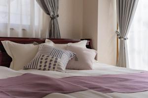 a bed with white pillows and purple sheets and a window at DAI HOSTEL Ayase in Fukaya