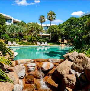 a swimming pool with chairs and a rock wall at Bugalmaa - Cotton Beach in Casuarina