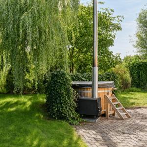 a wood fired spa in a garden with a tree at Villa Vera - Comfort, Space, Sauna & Hot Tub in Private Garden in Zeewolde