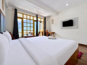 a white bedroom with a large white bed and a tv at Hotel Naina Rockland , Manali in Vashisht