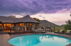 a swimming pool in front of a building with a tent at Tau Game Lodge in Madikwe Game Reserve
