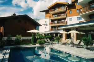 a hotel with a swimming pool with chairs and umbrellas at Venediger Lodge in Neukirchen am Großvenediger